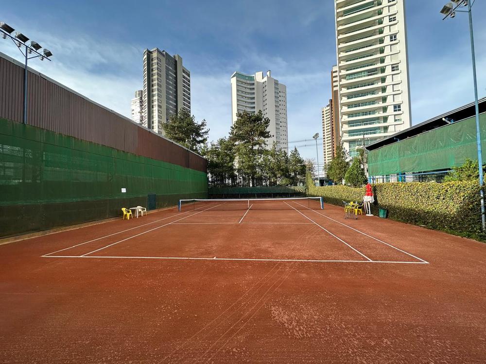 Quadra de saibro ao ar livre cercada por prédios e árvores